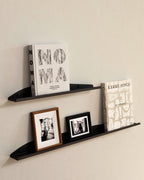 Two black slim metal wall shelves with books and framed prints