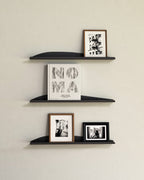 Three black slim metal wall shelves with books and framed prints
