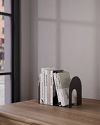 Black metal bookend holding upright books on a wooden shelf