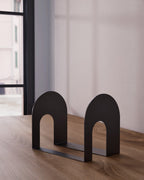 Black metal bookend with open arch shape on wooden shelf
