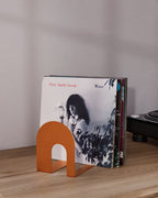 Orange metal bookend supporting vinyl records on a wooden shelf