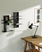 Two black modular metal shelves mounted on wall above desk