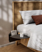 Black nightstand attached to wooden bed with coffee mug and book