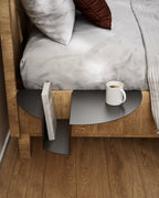 Black nightstand attached to wooden bed with coffee mug and book