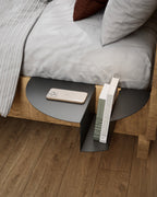 Black nightstand attached to wooden bed with phone and books