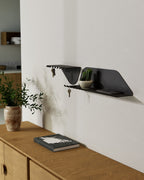 Black wall shelf with hooks holding keys above wooden console