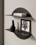 Black round metal wall shelf with books, vase, and framed print