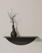 Black round metal wall shelf with vase on textured wall