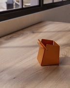 Orange metal pen holder with folded front edge on desk