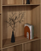 Orange metal bookend holding upright books on a wooden shelf