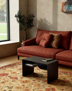 Black metal coffee table with book rack in front of rust sofa