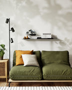 Two black slim metal wall shelves above green sofa with books and decor