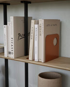 Orange metal bookend supporting books on a wooden shelf