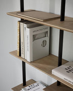 White metal bookend holding large books on a wooden shelf