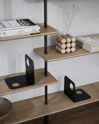 Black metal bookends on wooden shelves with books and decorative objects