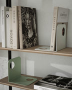 White and green metal bookends on wooden shelves with books