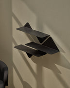 Close-up of two black modular metal wall shelves mounted on wall